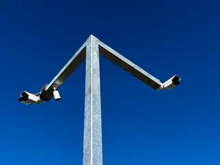 Two CCTV cameras on a galvanised pole against a blue sky