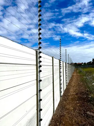 Electric fencing along a long white precast wall