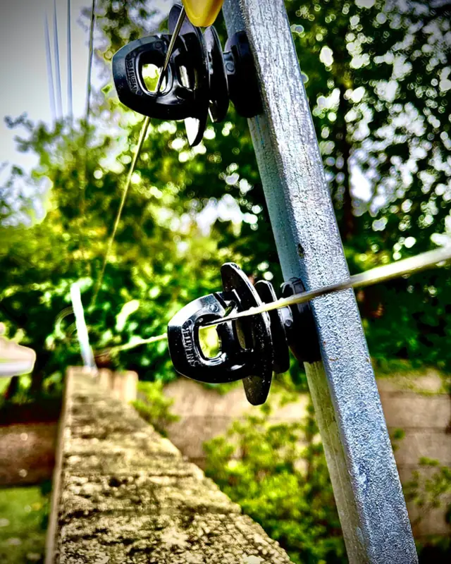Close-up of electric fence insulators and wires on a galvanised post