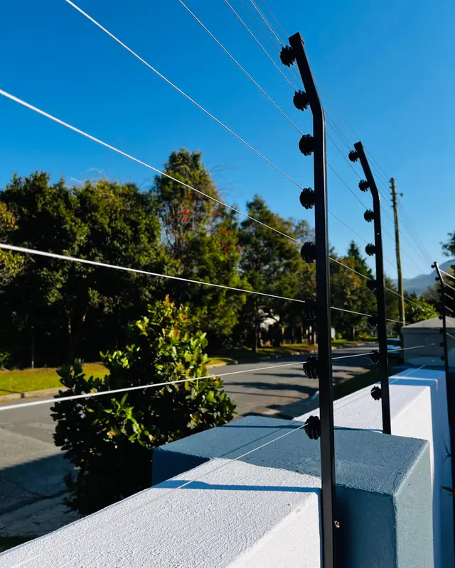 Electric fence brackets on a wall with trees and blue sky