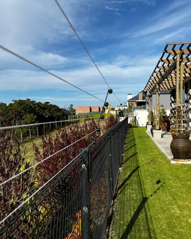 Electric fence wires along a garden boundary with a pergola